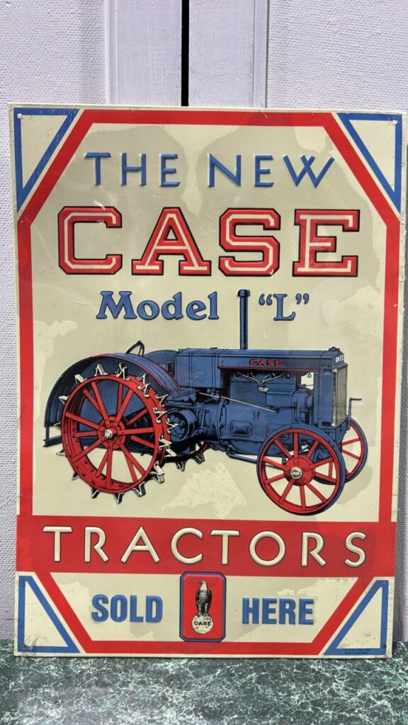 Rectangular Metal Sign that reads The New Case Model "L" Tractors. The background is cream coloured with a thin red outline around the perimeter of the sign. Inside the tractor is an olf=d fashioned Blue tractor with Red steel wheels