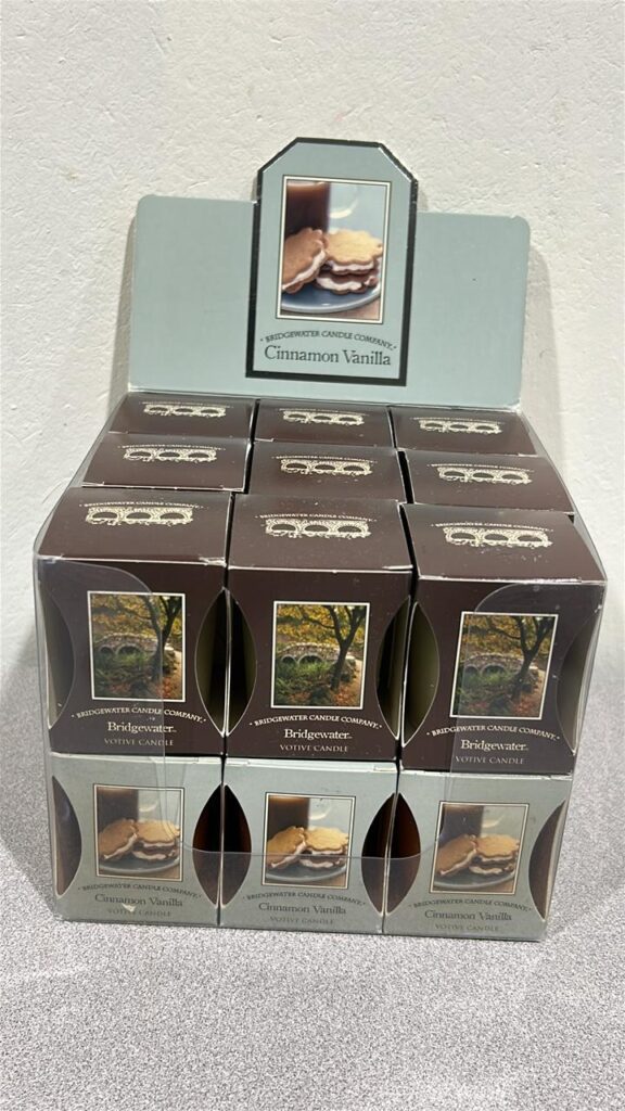 Display box of 18 Bridgewater votive candles that are individually packaged. They are 9 of the Bridgewater scent in brown boxes, 9 in gray boxes that are Cinnamon Vanilla Scent