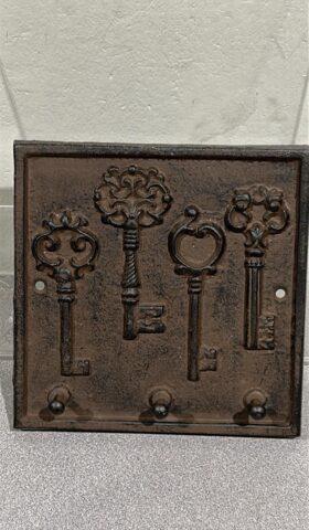 Square shaped Cast iron plaque that has 4 Vintage door keys embossed on the plaque in the middle of the rectangle. 3 hooks for keys spaced out along the bottom edge